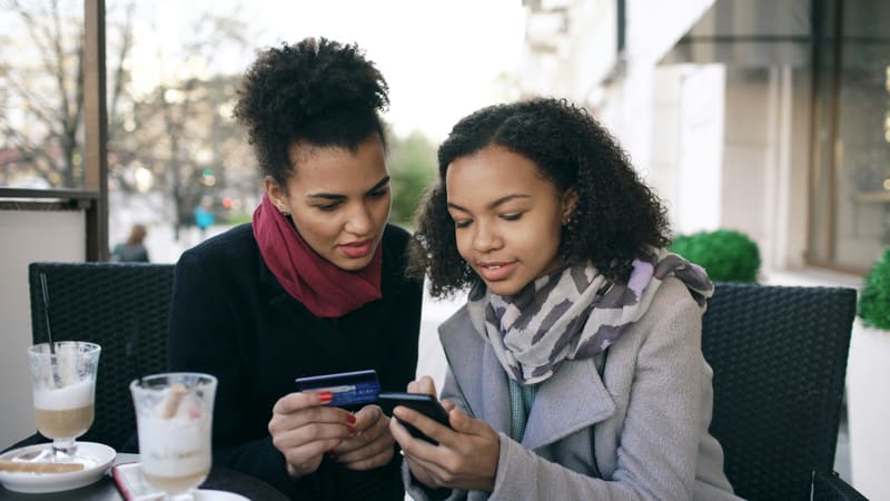 Zwei Freundinnen teilen sich beim Café-Besuch die Rechnung per Smartphone
